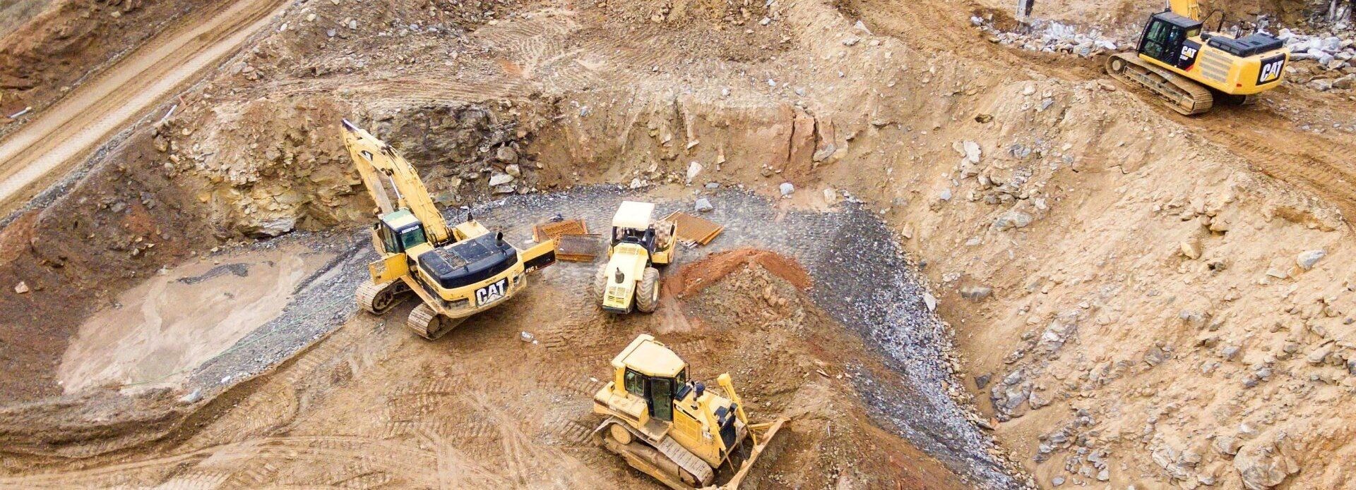 Luftaufnahme einer aktiven Baustelle mit mehreren schweren Maschinen, darunter Bulldozer und Bagger, auf ausgehobener Erde.